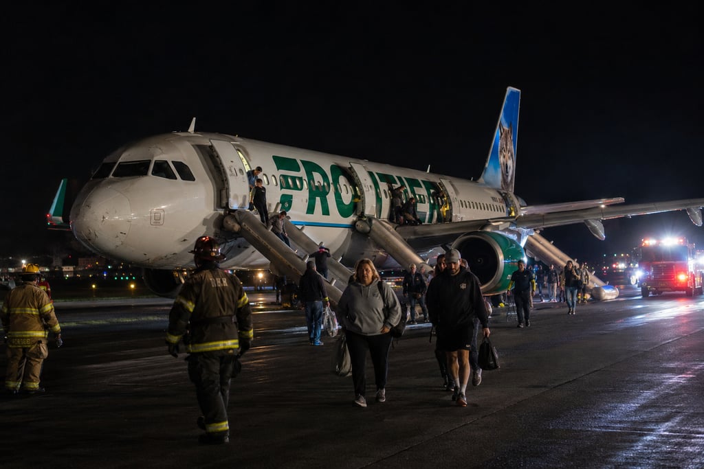 Passengers evacuate a Frontier Airlines plane using emergency slides on a runway at night.