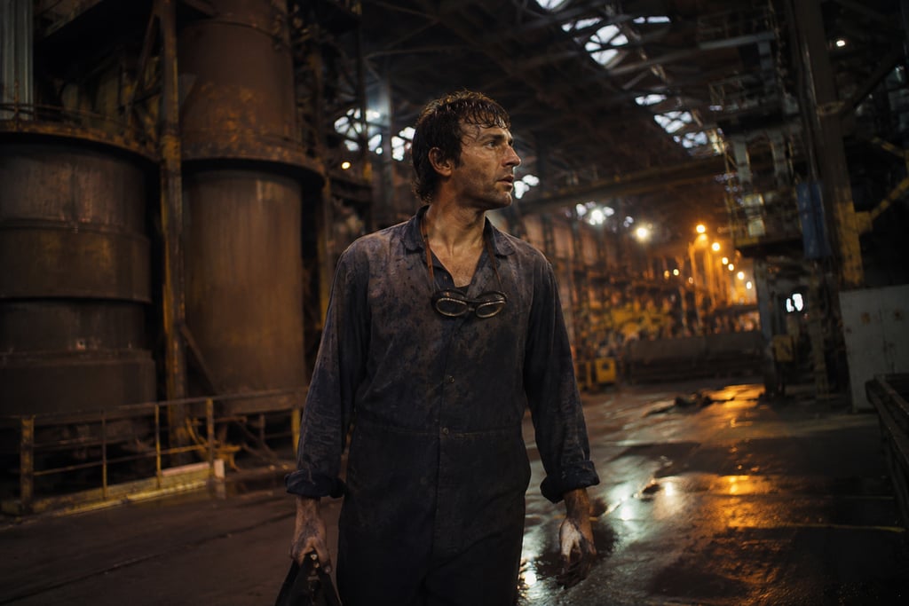 A gritty industrial worker in a dark steel mill wearing blue overalls and safety goggles.