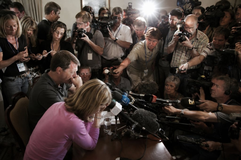 A crowd of journalists and news photographers with cameras surrounding a couple at a press conference.