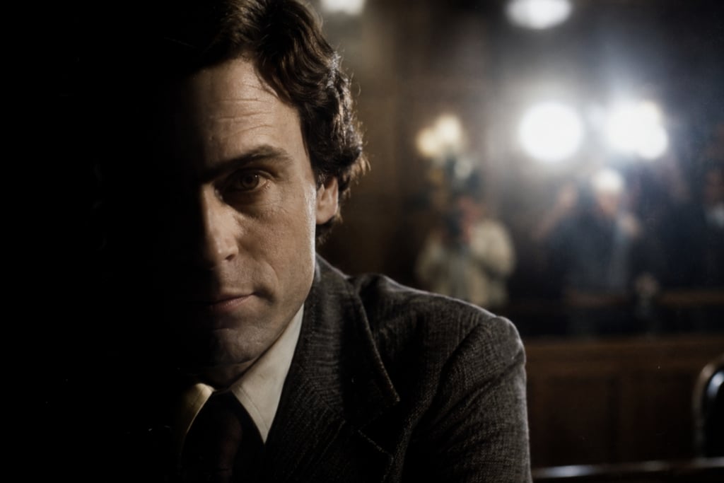 Close-up of Ted Bundy in a courtroom with camera flashes and reporters in the background.