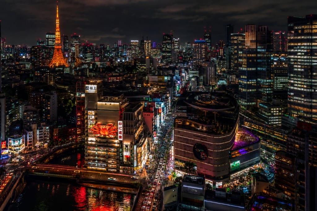Aerial night view of Tokyo city skyline featuring the illuminated Tokyo Tower and busy city streets.
