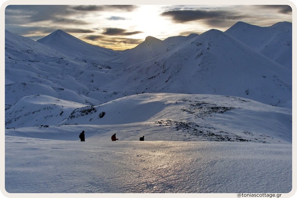 People hiking across a vast snowy mountain landscape at sunset in Crete