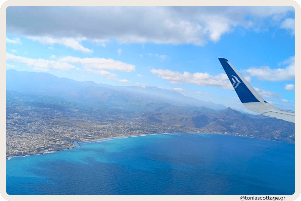 View of Crete from an airplane window, showcasing the deep blue sea and rugged mountains