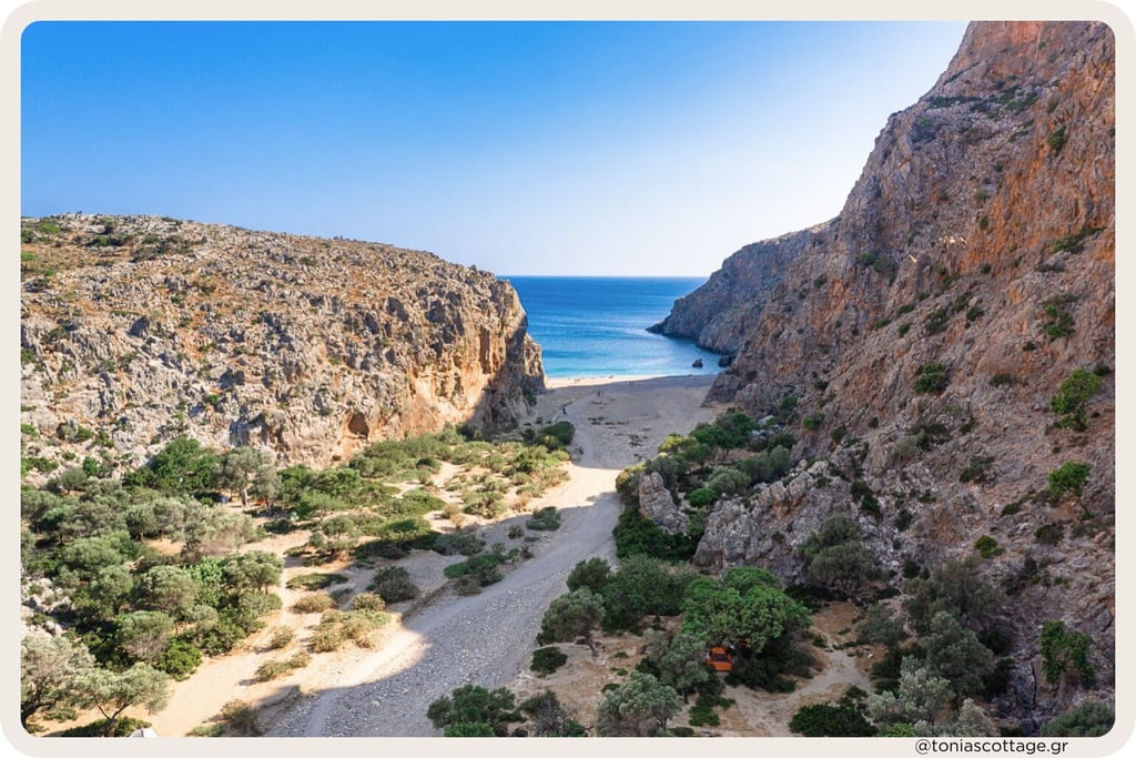 Agiofarrago Gorge in Crete, with high rocky walls, some trees, and a quiet beach meeting the sea
