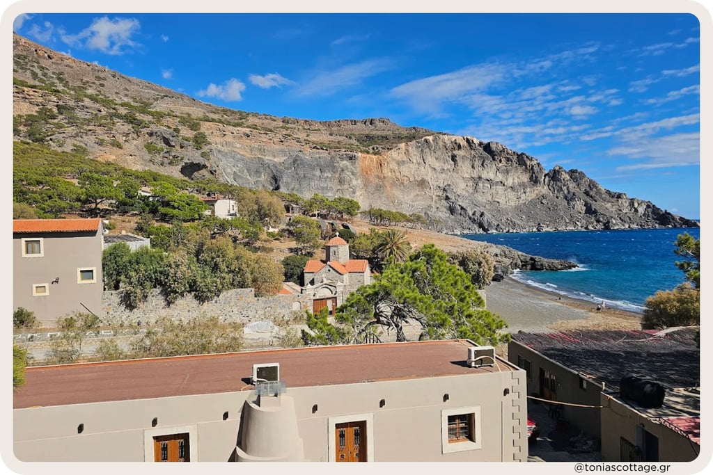 Koudoumas Monastery perched on rolling hills surrounded by green shrubland and dry rocky terrain.