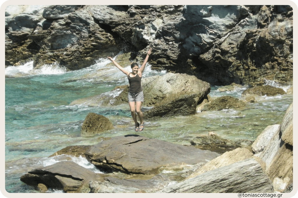 Tonia with raised arms standing on coastal rocks by clear turquoise sea in Crete