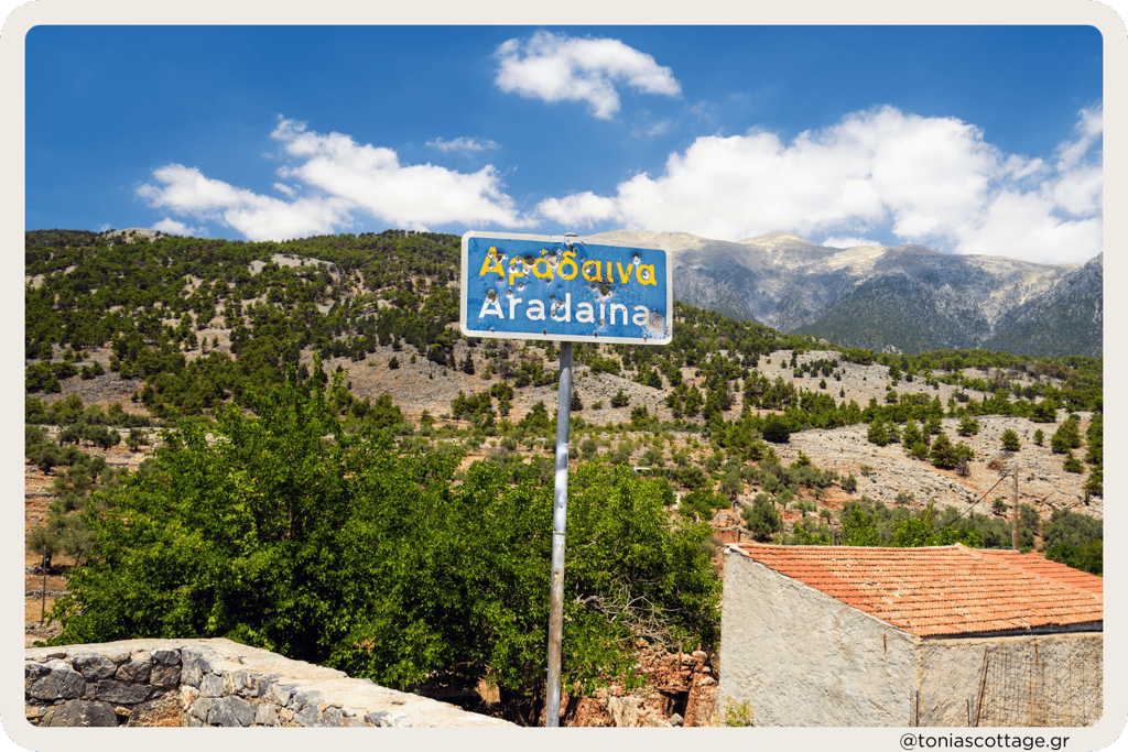A street sign with bullet holes, set against the backdrop of the mountains in Aradena, Crete
