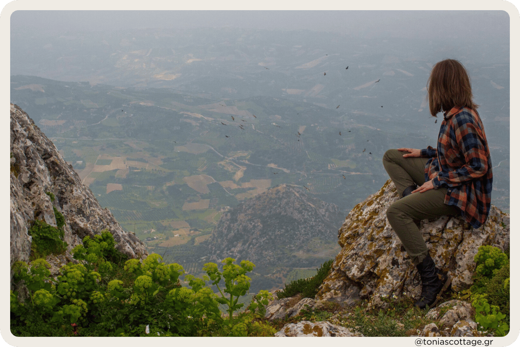 Woman sitting with a view of the valley in the mountains of Crete, surrounded by nature