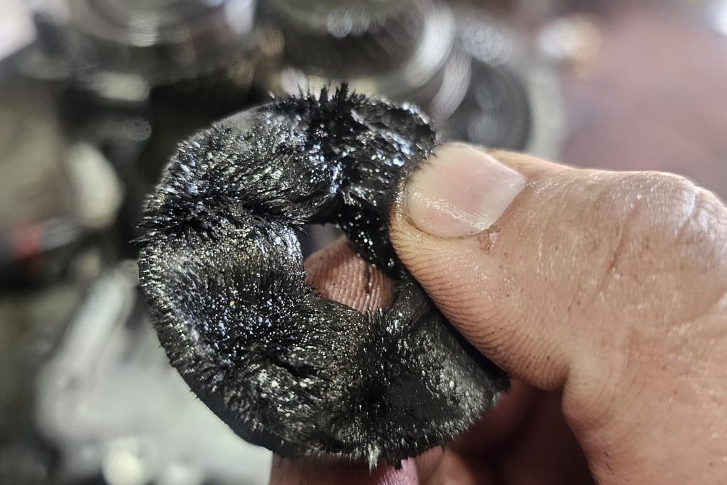 A mechanic holding a magnetic drain plug covered in metal shavings from a vehicle transmission.