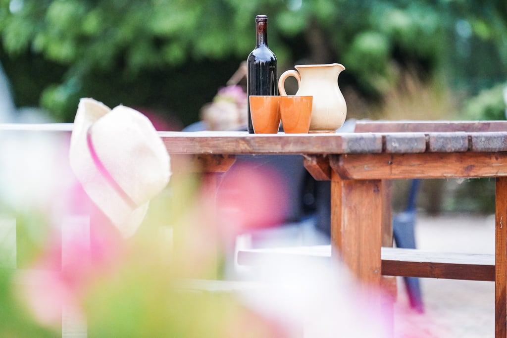 Tavolo nel giardino dell'agriturismo con sopra una caraffa, vino locale e bicchieri in terracotta