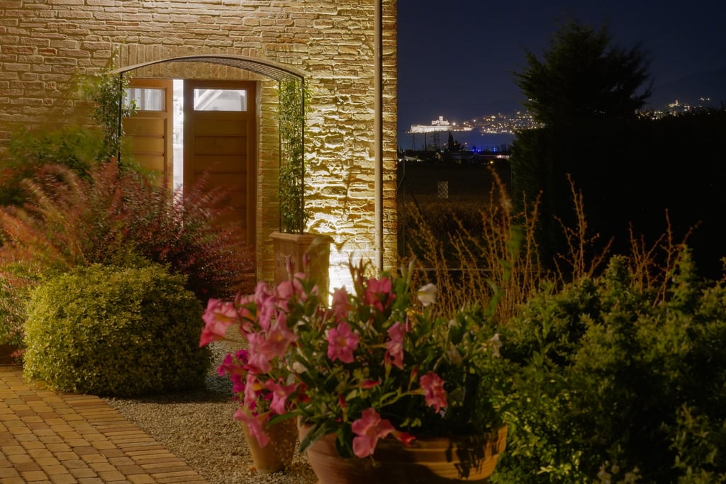 Esterno dell'agriturismo di sera, con fiori del nostro giardino e una romantica veduta su Assisi