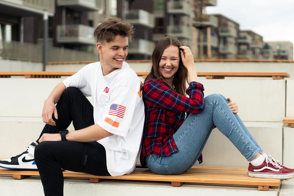 Lachendes Paar sitzt Rücken an Rücken auf einer Bank. Urbanes Paarfoto von Just Perspectives.