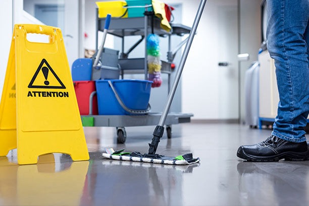 Professional janitor mopping a commercial floor next to a yellow wet floor caution sign.