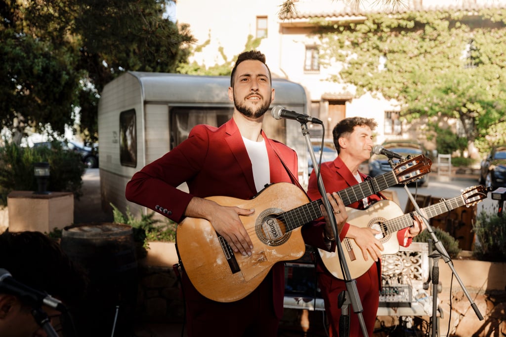 Live wedding musicians in red suits playing acoustic guitars and singing at an outdoor reception.
