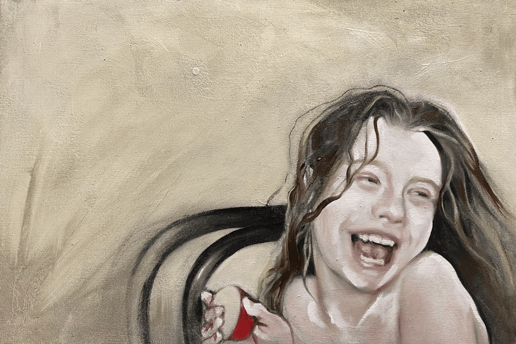 Head and shoulders of a young girl with long hair sitting on a chair laughing, holding an apple.