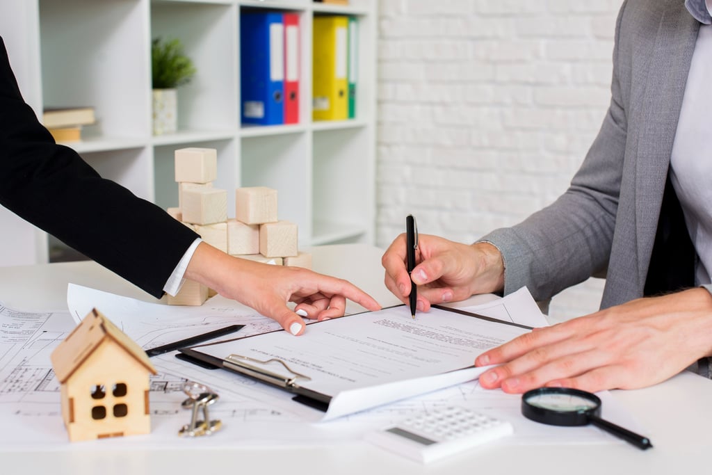 Signature d'un contrat immobilier avec une maquette de maison et des documents sur la table.