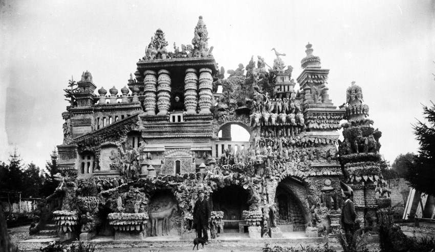 Vintage black and white photo of Ferdinand Cheval standing before Palais Idéal, his intricate pebble stone palace.