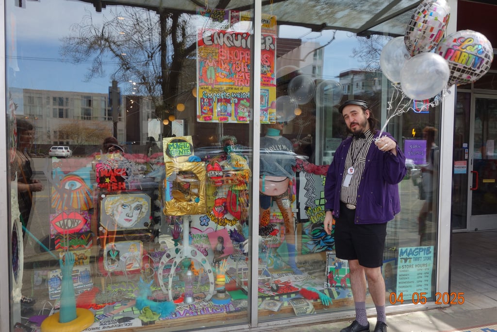 Magpie staff member holding balloons and standing in front of a storefront window filled with art