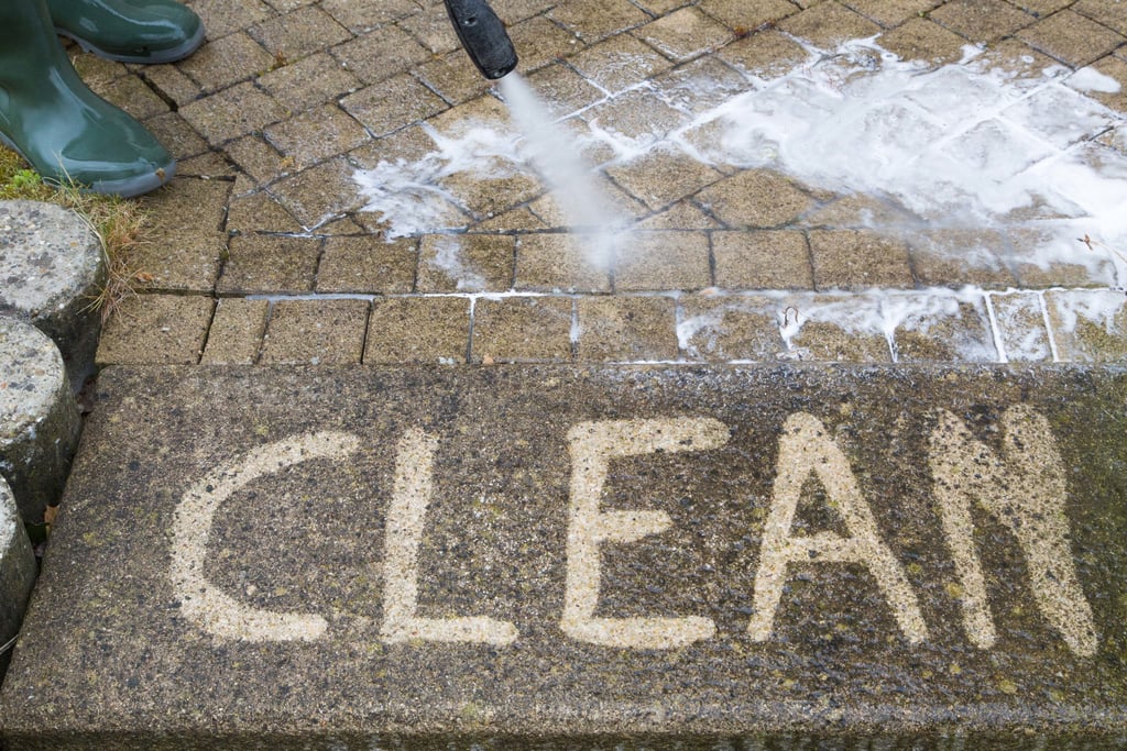 A man pressure washing with "clean" having been writen onto the sidewalk with the pressure washer