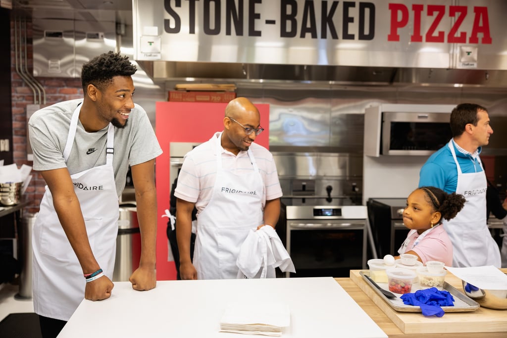 Smiling group wearing Frigidaire aprons in a stone-baked pizza kitchen during a cooking class.