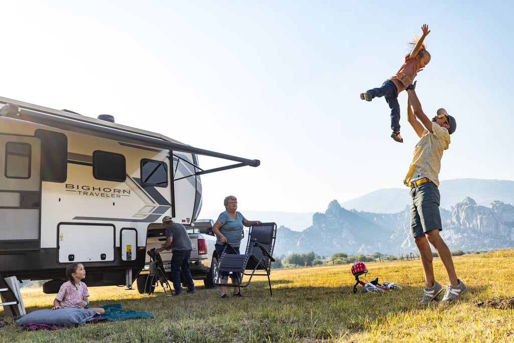 A multi-generational family enjoys an RV camping trip in the mountains while a father lifts his child.