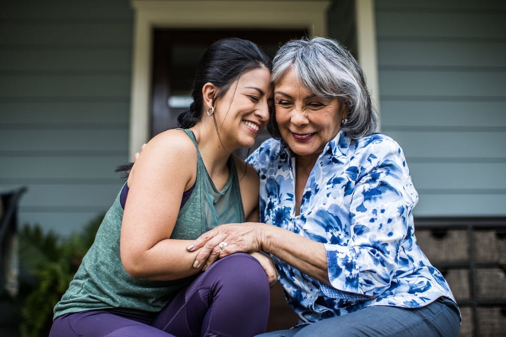 Smiling senior Hispanic mother and adult daughter hugging and sharing a tender moment together outdoors.