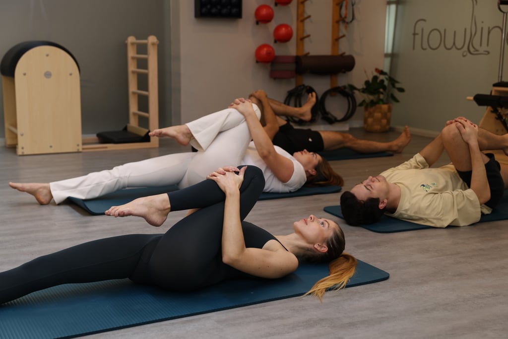 Quatro pessoas deitadas em tapetes num estúdio de Pilates, alongando  em posição single leg stretch