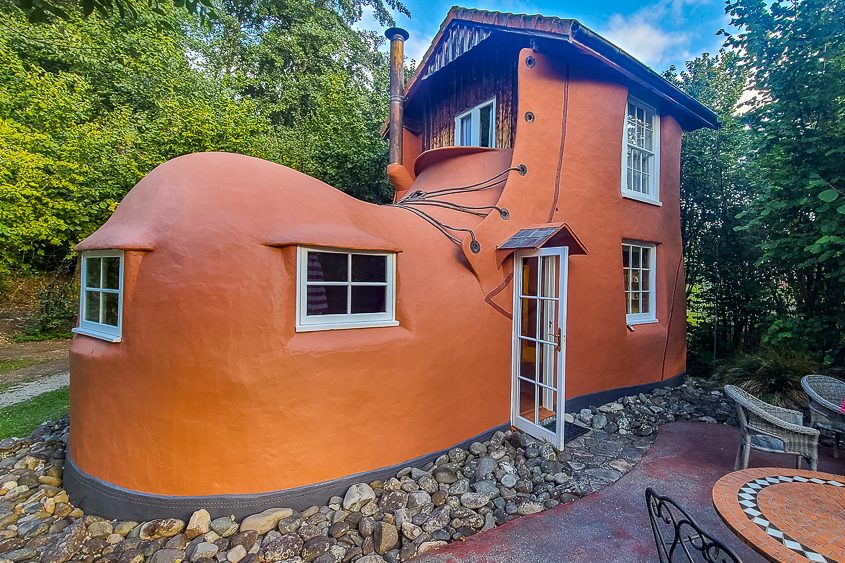 A whimsical giant orange shoe house cottage with windows and a door nestled in a lush green forest.