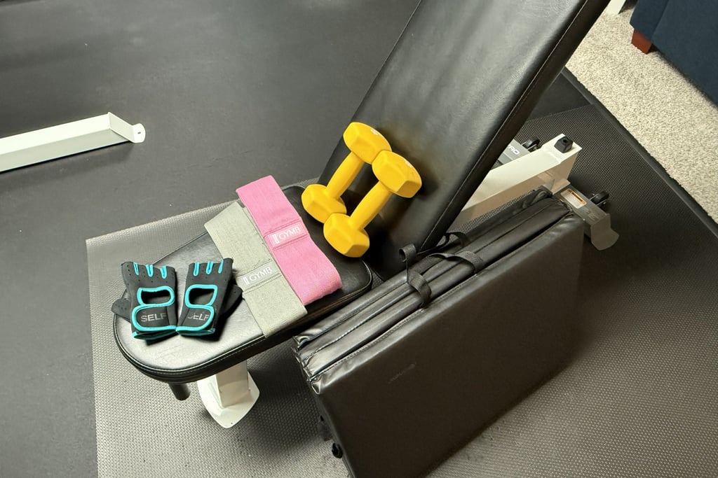 Home gym setup with a bench, dumbbells, resistance bands, a mat, and workout gloves.