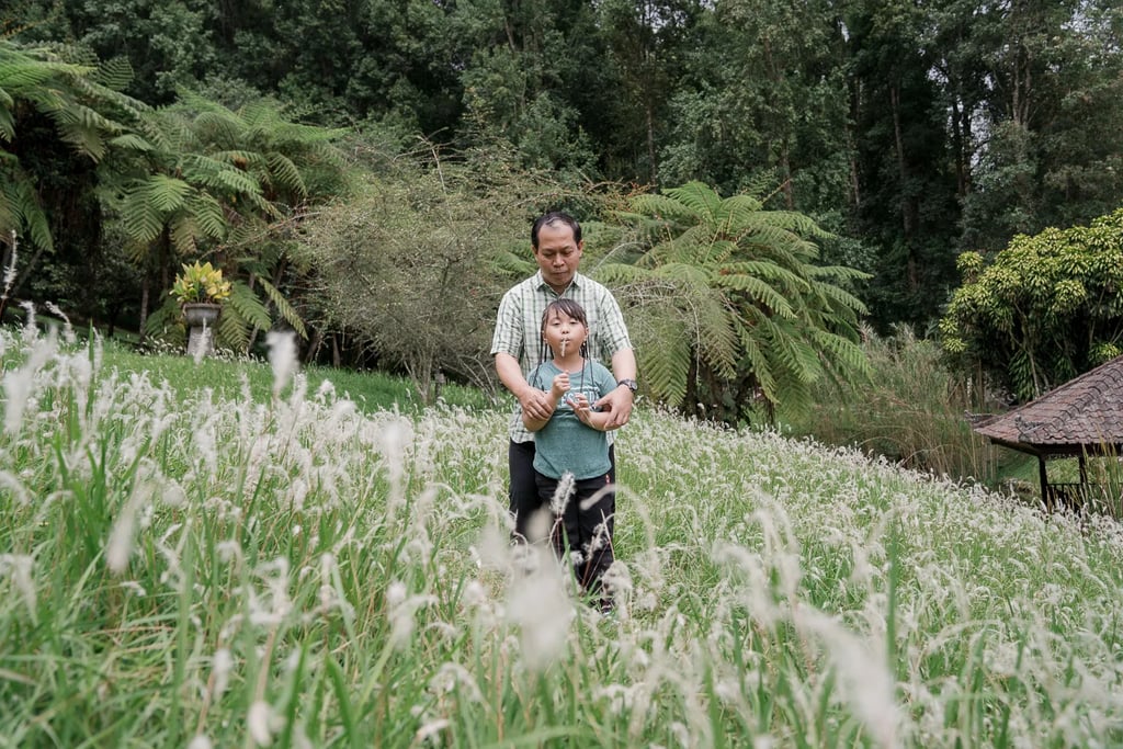 Father and son walking through a scenic grass field during a family photography session in Bedugul Bali.