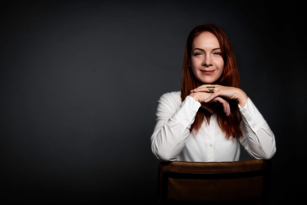 Professional corporate headshot of a smiling redhead woman in a white blouse on a dark background.