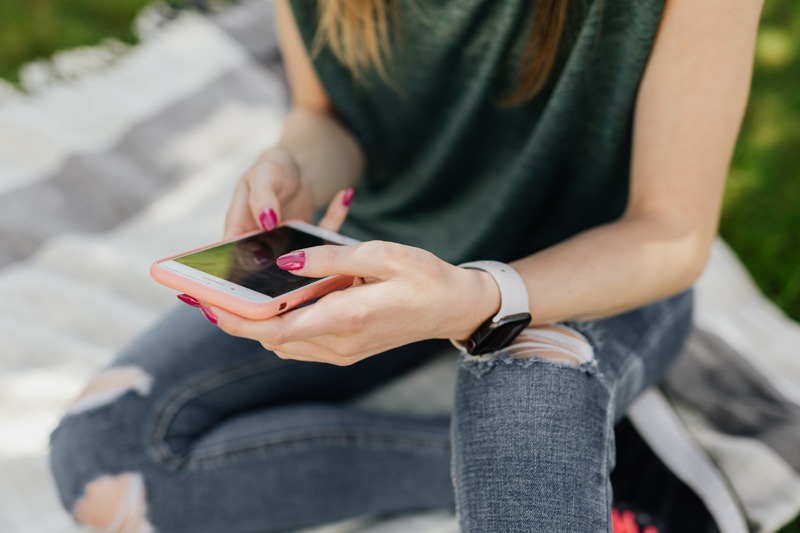 Photo of an adolescent girl with ripped jeans using a smartphone