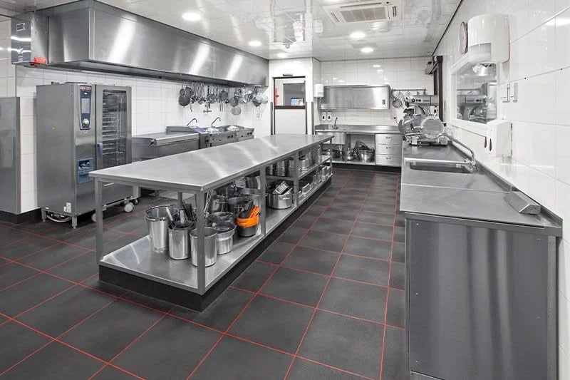 A large stainless steel table with multiple storage shelves used as a central workstation in a commercial kitchen.