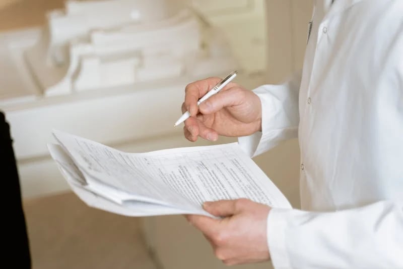 un hombre con bata blanca sosteniendo un bolígrafo y unos documentos clínicos