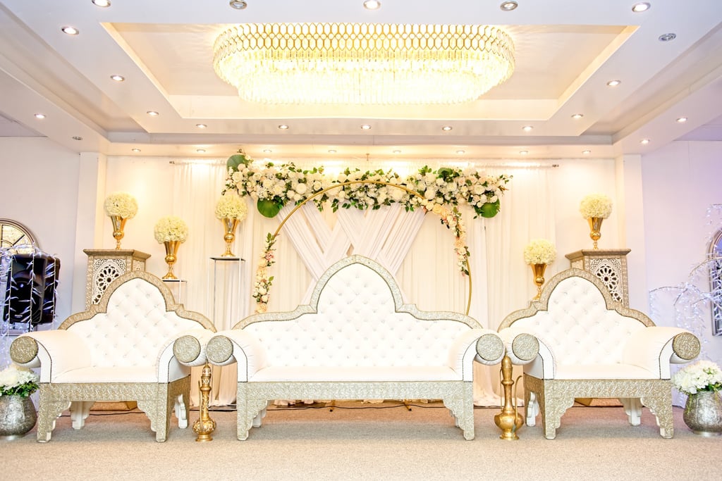 inside wedding venue, regal white chairs, flowers and draping background, large chandelier in centre