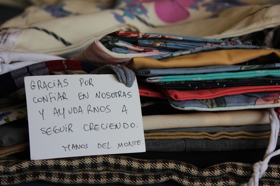 Handwritten thank you note on a stack of folded handmade textile clothing and patterned fabrics.