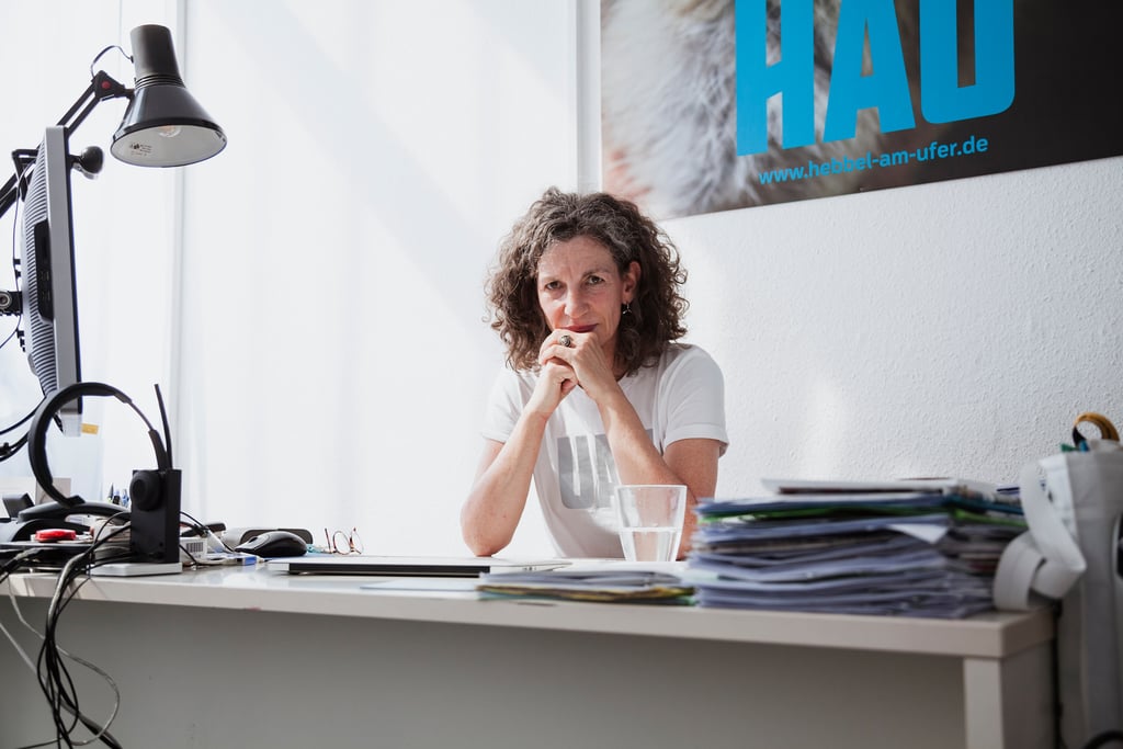 Annemie Vanackere, fotografiert in ihrem HAU-Büro hinter einem Schreibtisch.