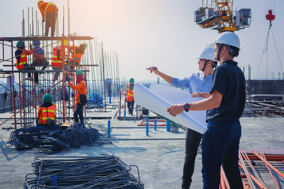 two men in hard hats and safety vests standing in front of a building