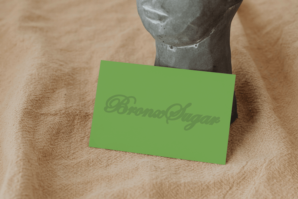 Green Bronx Sugar business card resting against a stone face statue on textured beige fabric.