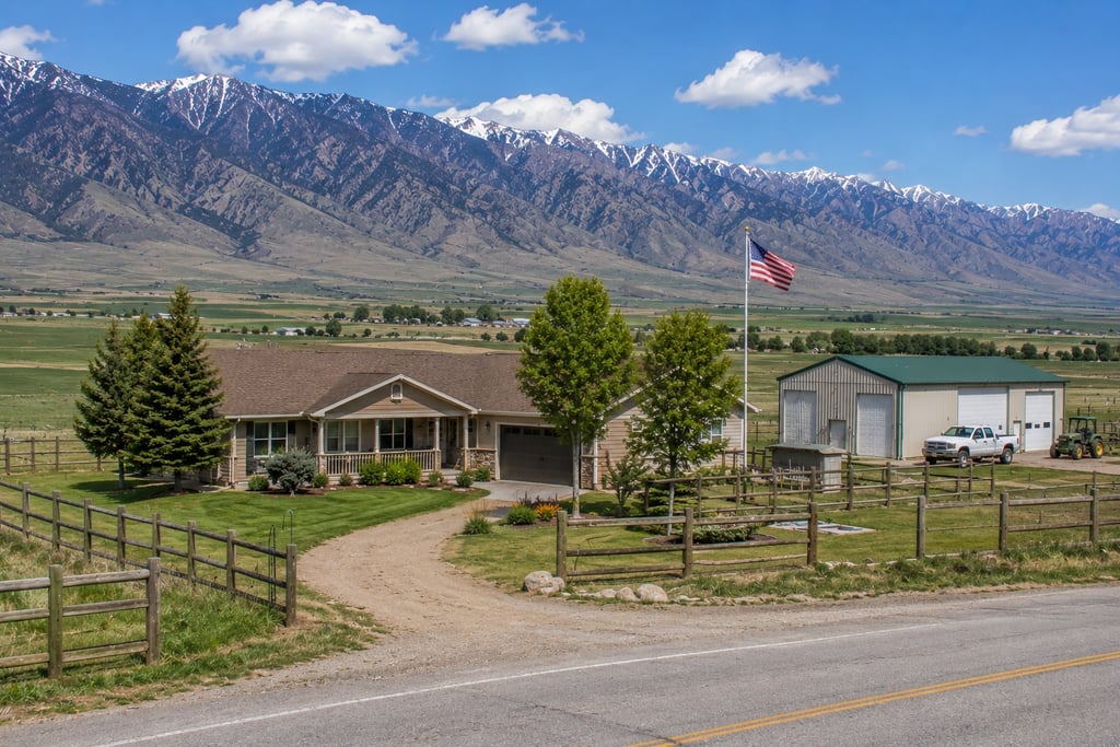 A scenic mountain ranch home with a large detached workshop, fenced yard, and American flag.