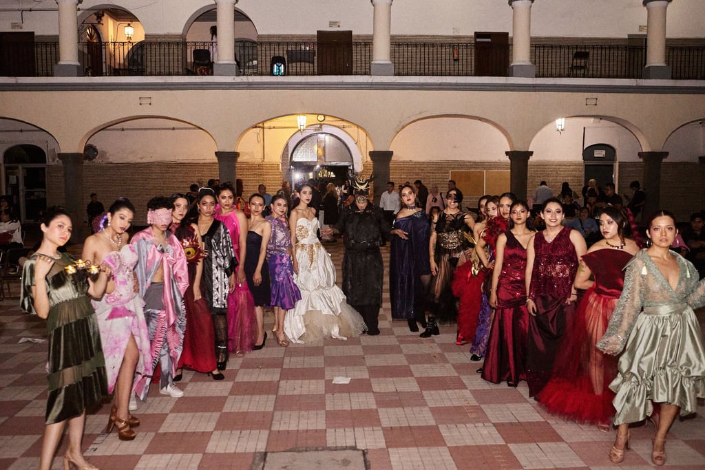 Fashion models posing in avant-garde designer gowns and creative costumes at an outdoor evening runway show.