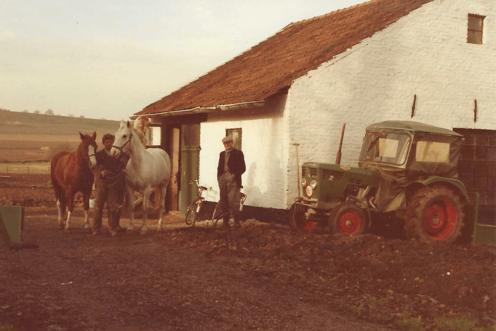 Historische foto van Hoeve Dinjens in Maastricht met een man, paarden en tractor voor de boerderij.