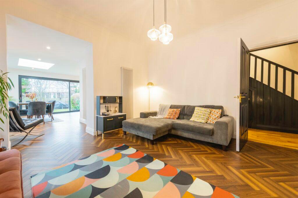 Modern living room with herringbone wood flooring, a grey corner sofa, and a colorful geometric rug.