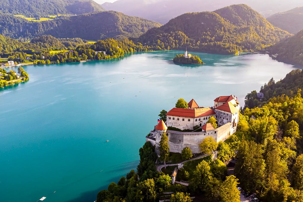 Aerial view of Bled Castle overlooking turquoise Lake Bled and the Pilgrimage Church of the Assumption in Slovenia.