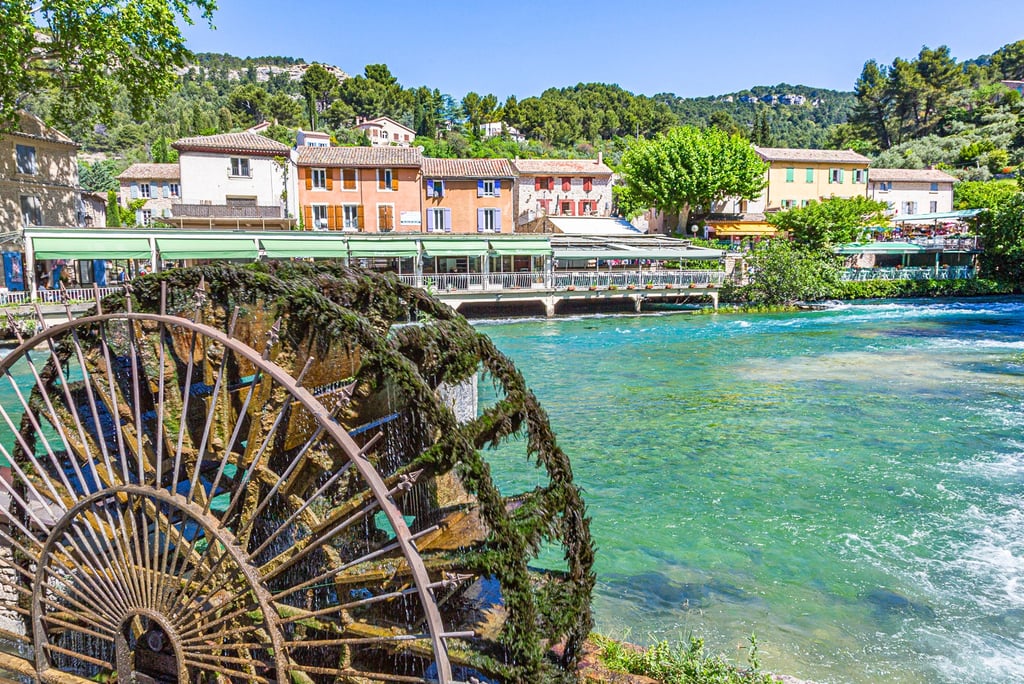 A moss-covered antique water wheel turns in the Sorgue River near waterfront cafes in Fontaine-de-Vaucluse, France.