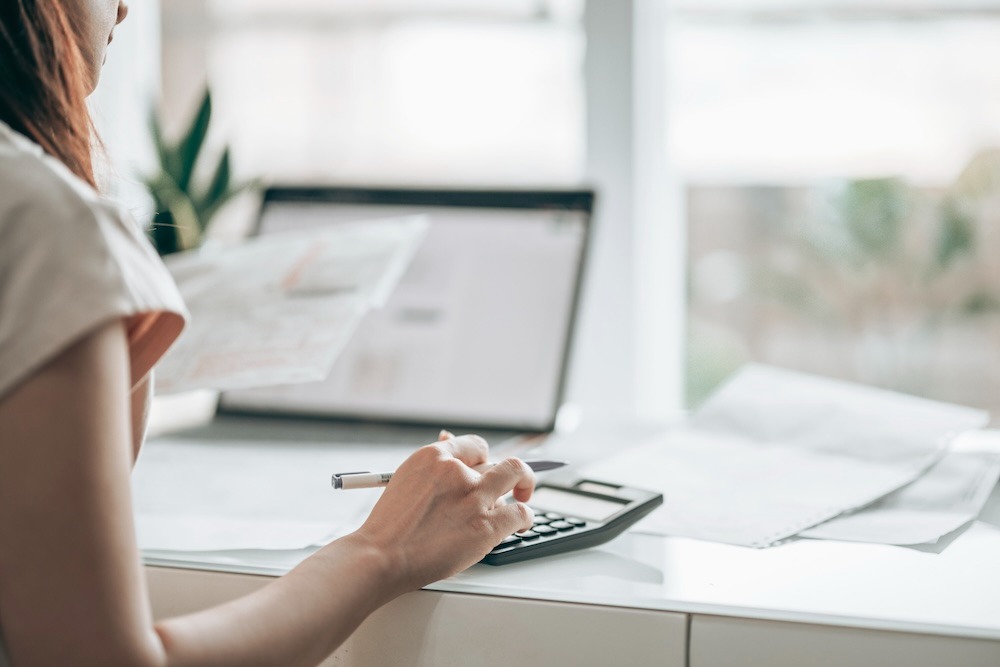 Woman managing monthly bookkeeping, using a calculator and computer to organize financial records.