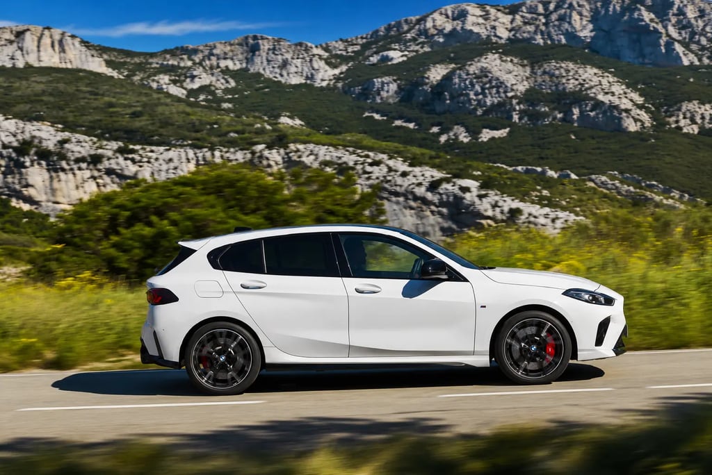 BMW hatch branco em movimento por estrada cercada por montanhas e vegetação