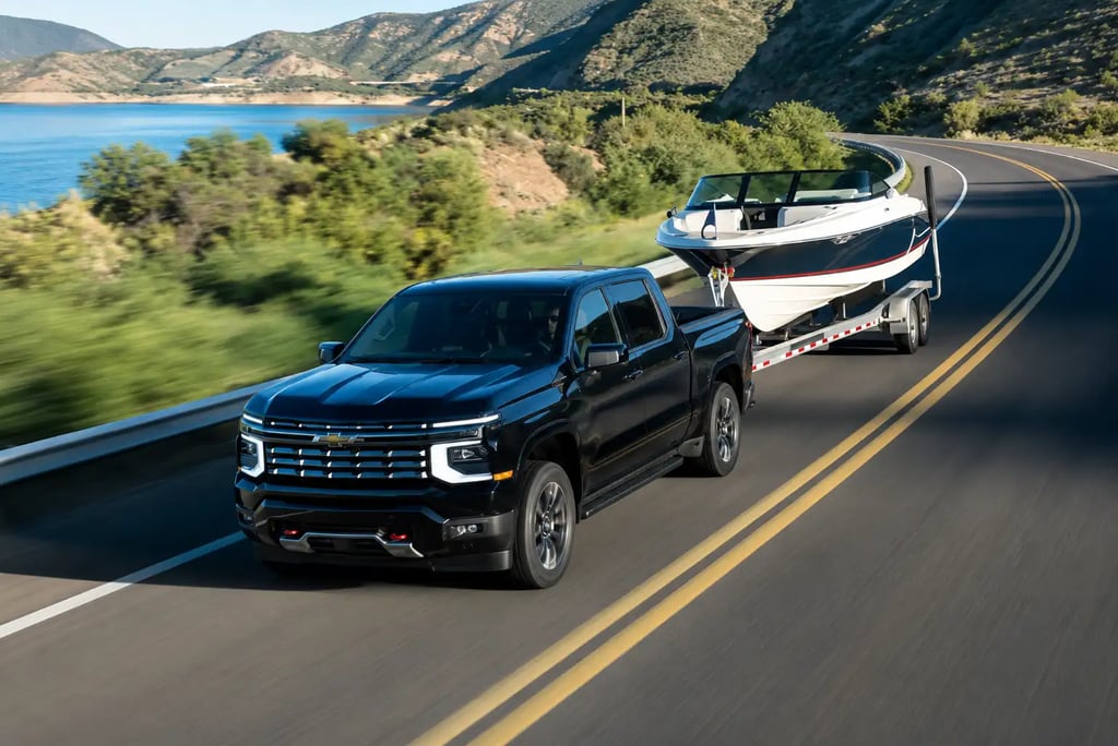 Chevrolet Silverado rebocando lancha em rodovia sinuosa à beira de lago e montanhas.