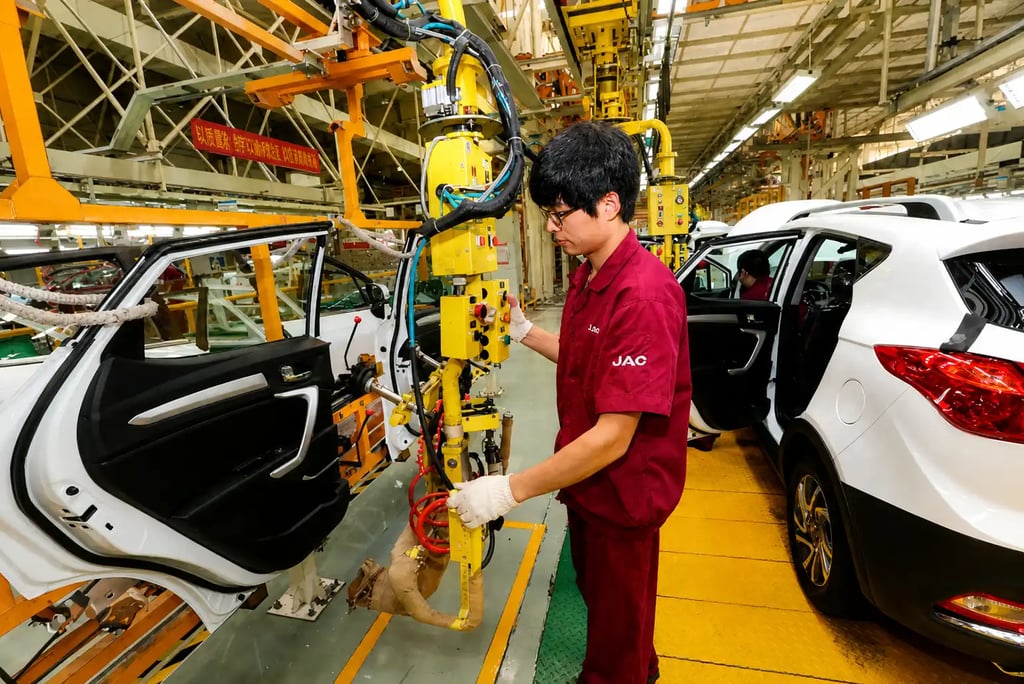 Operário em fábrica de carros na China trabalhando na linha de montagem automatizada com veículos em