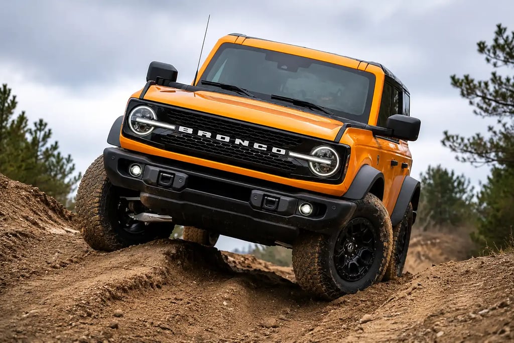 Ford Bronco laranja encarando trilha off-road em terreno irregular